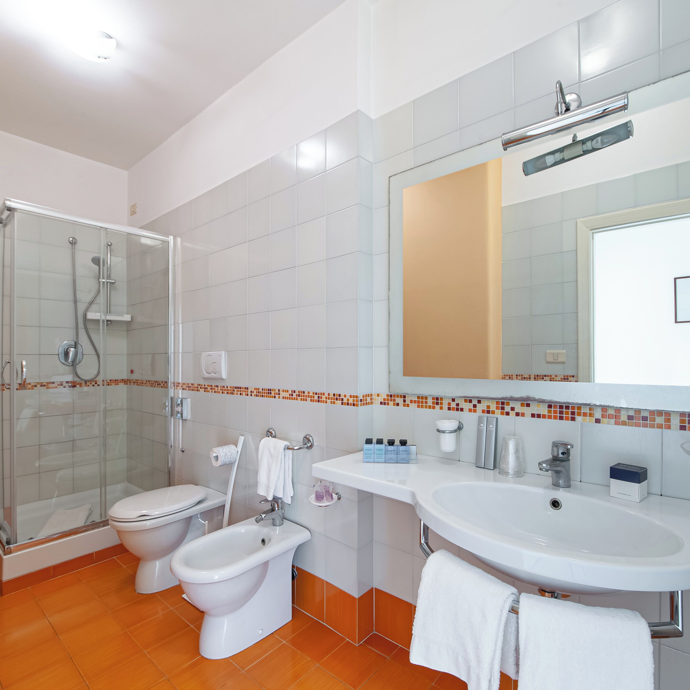 Un baño moderno con ducha de vidrio, inodoro, bidé y lavamanos con espejo.