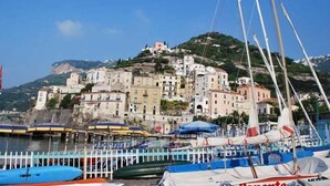 A coastal town with buildings on a hillside, a marina with boats, and a clear blue sky. - Palazzo Vingius (Minori)