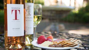 Two wine bottles, a plate with strawberries, cheese, and crackers, and a glass of white wine on a metal table.