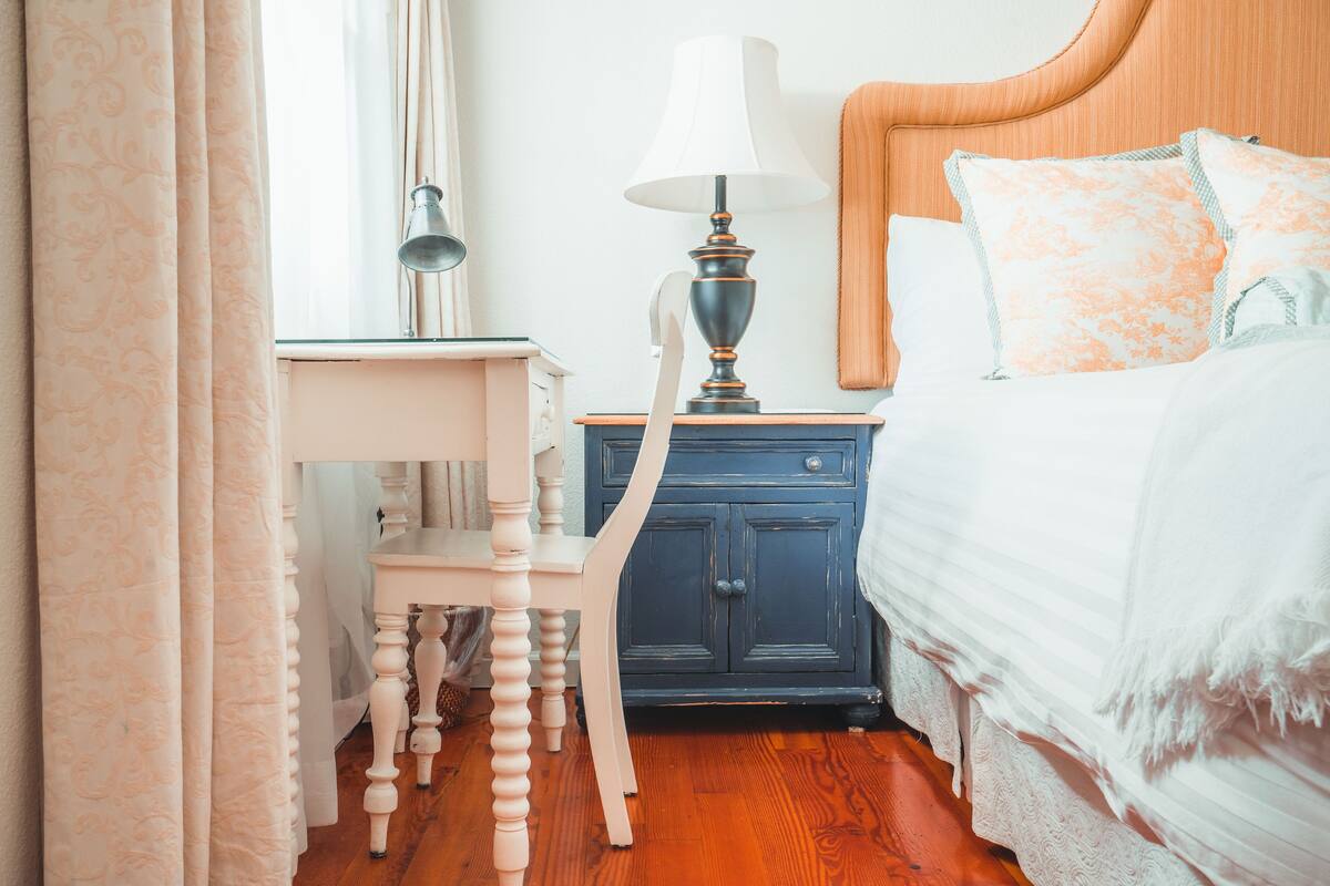 A bedroom with a wooden headboard, a bedside table with a lamp, a nightstand, and a bed with patterned pillows.