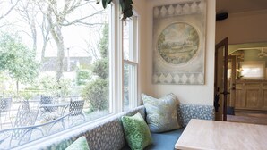 A cozy seating area with a view of the garden, a painting on the wall, and a glimpse of the kitchen. - Cottage Grove Inn (Calistoga)