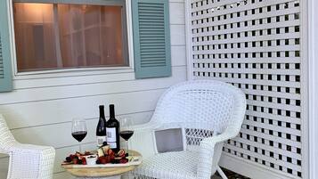 A patio with two white wicker chairs, a small round table, and a bottle of wine.