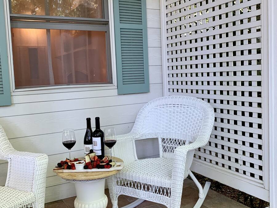 A patio with two white wicker chairs, a small round table, and a bottle of wine.