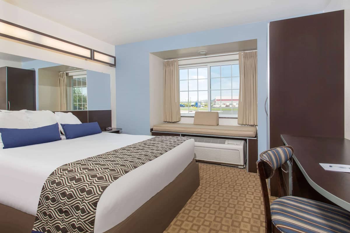 Habitación de hotel con una cama grande, un escritorio con silla, una ventana con cortinas y vistas al exterior.