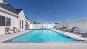 A rectangular swimming pool with a tiled edge, surrounded by a white fence, and adjacent to a building with large windows and a door.