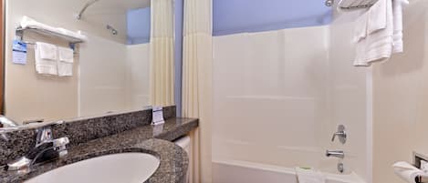 Un baño moderno con lavamanos de granito, inodoro blanco, bañera y ducha con puerta de vidrio.
