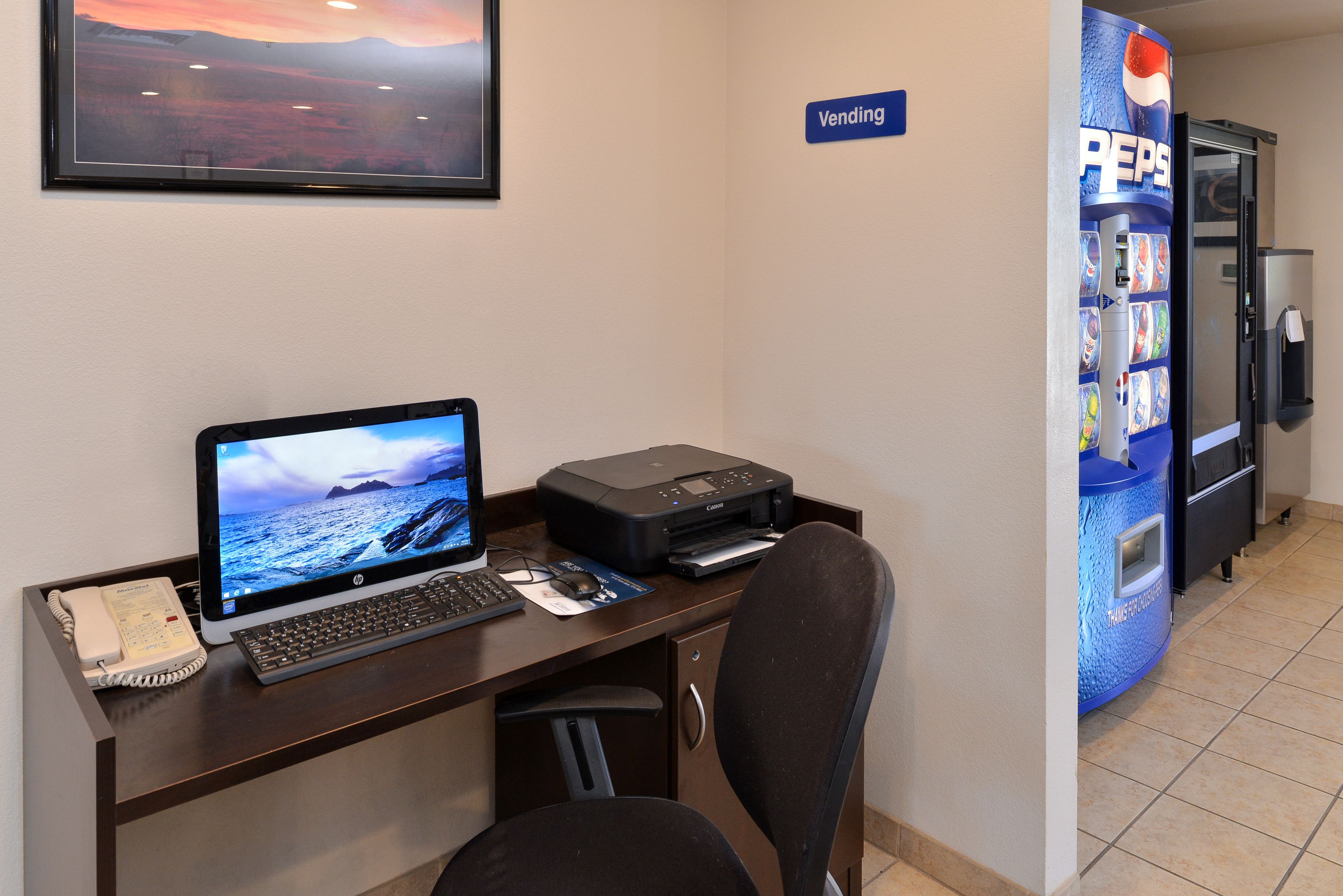 A desk with a computer, printer, and phone, a vending machine, and a "Vending" sign.