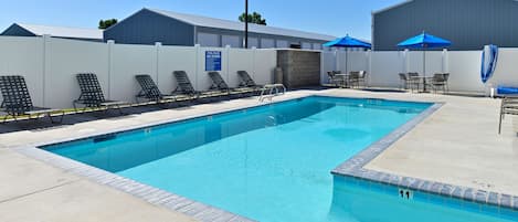 A swimming pool with lounge chairs and umbrellas, surrounded by a white fence and a building.