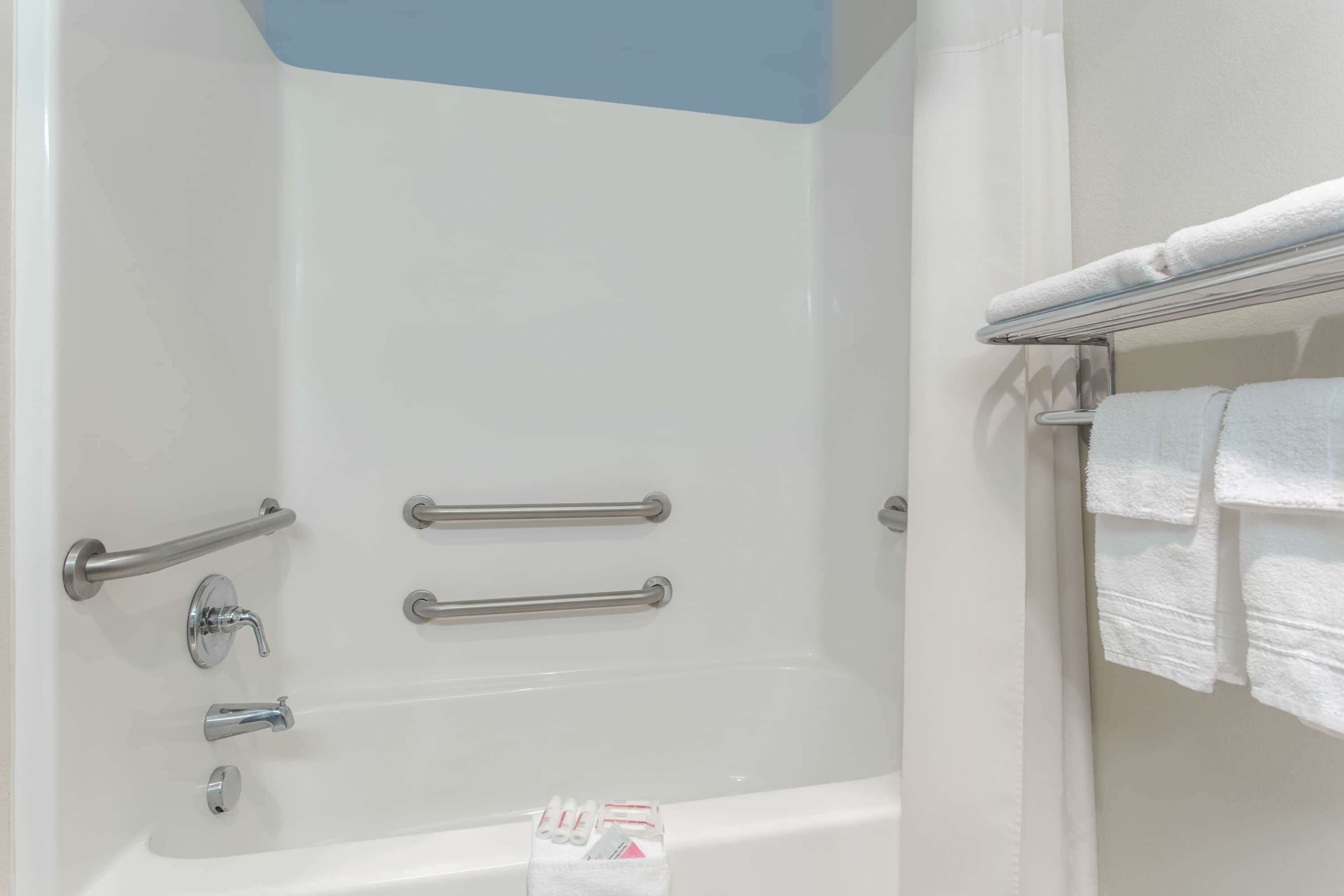 Un baño moderno con bañera, barras de apoyo y un perchero para toallas.