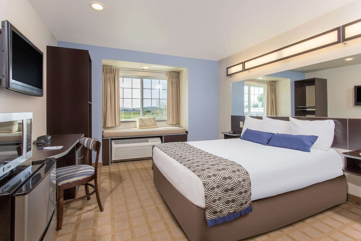 Una habitación de hotel con una cama, un escritorio, una silla, un televisor y una ventana con cortinas.