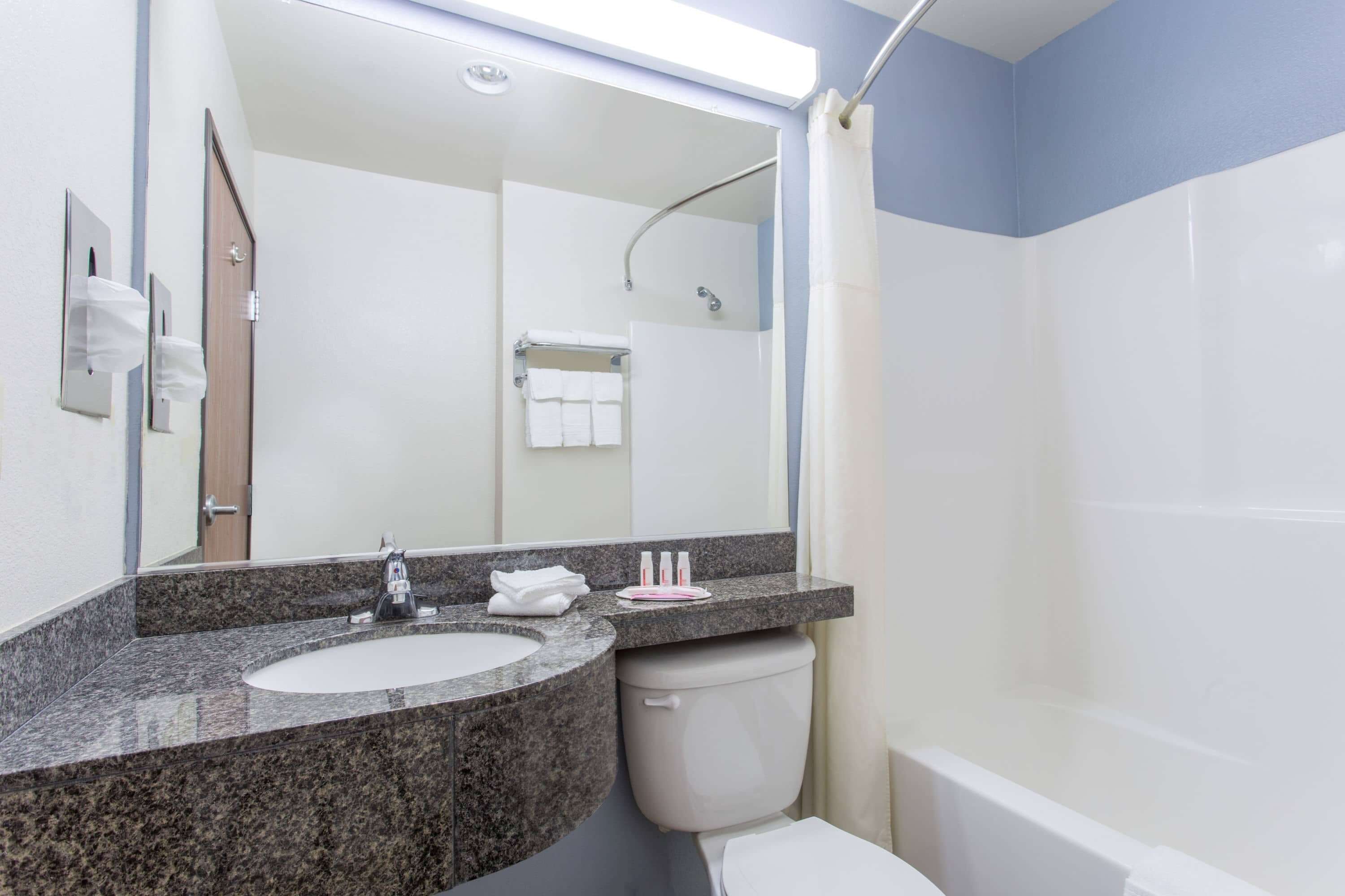Un baño con lavamanos de granito, un espejo, inodoro y zona de ducha.
