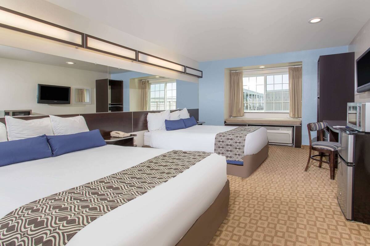 Habitación de hotel con dos camas, un escritorio, una silla, un televisor y un ventanal grande.