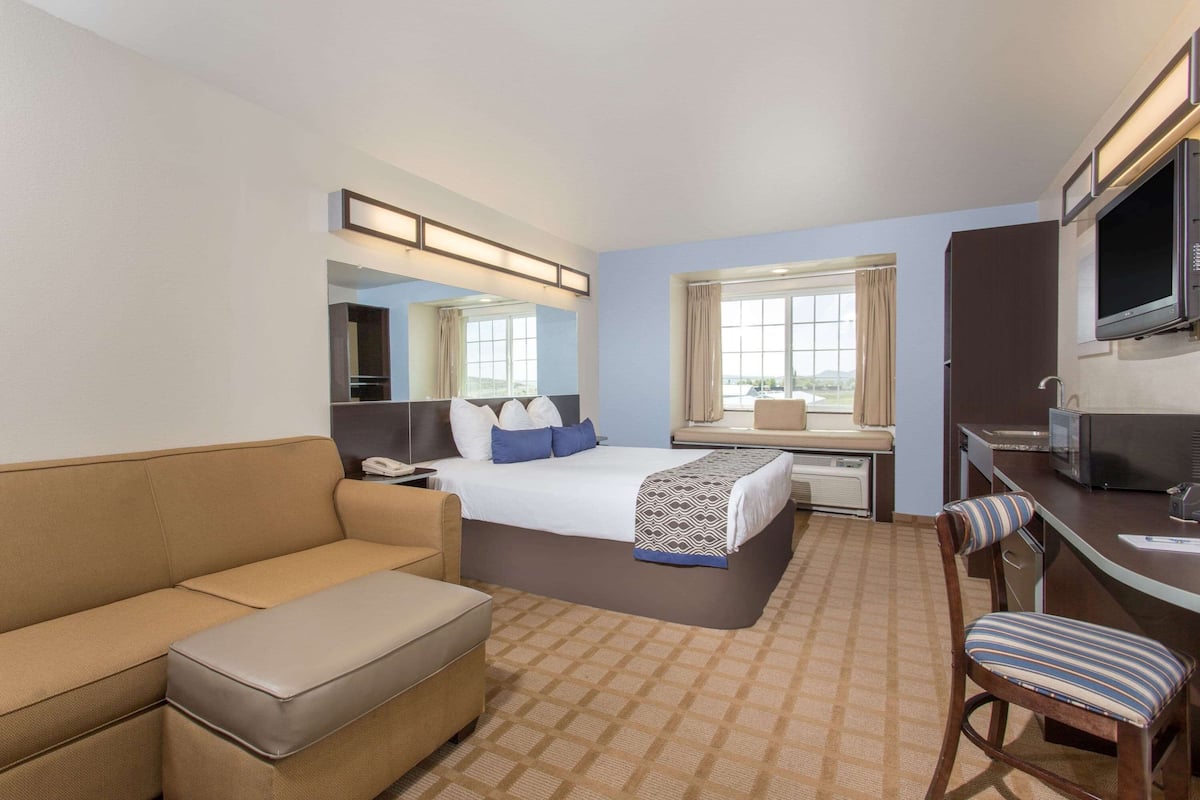 Habitación de hotel con cama, sofá, escritorio con silla, televisión y ventana con cortinas.