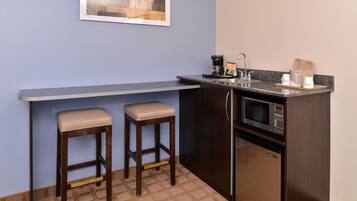 A compact kitchen with a built-in microwave, a coffee maker, and two bar stools.