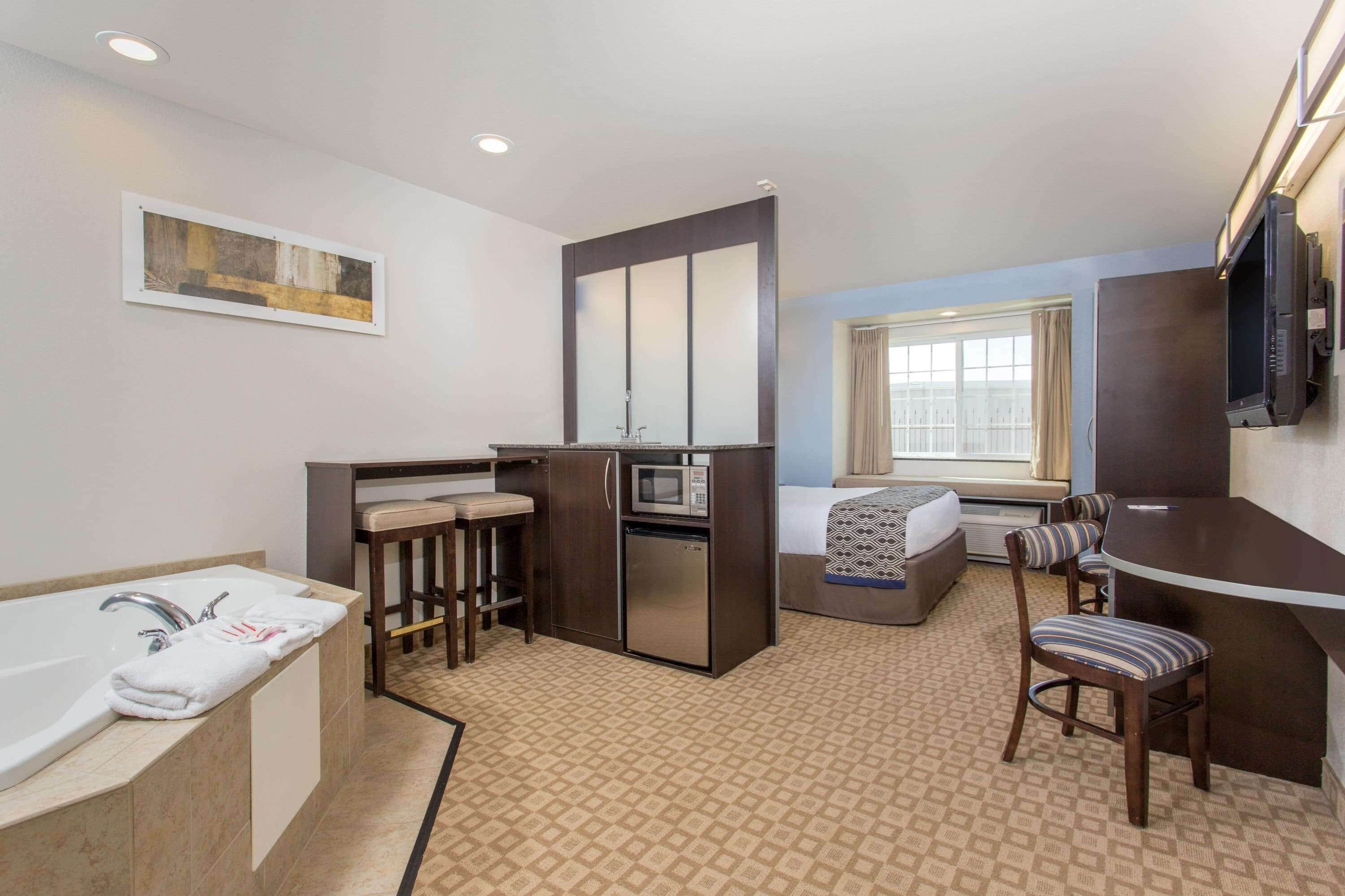A compact hotel room with a bathroom, a small kitchenette, a bed, and a seating area.