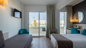Habitación de hotel con dos camas, televisión, escritorio y balcón con vistas.