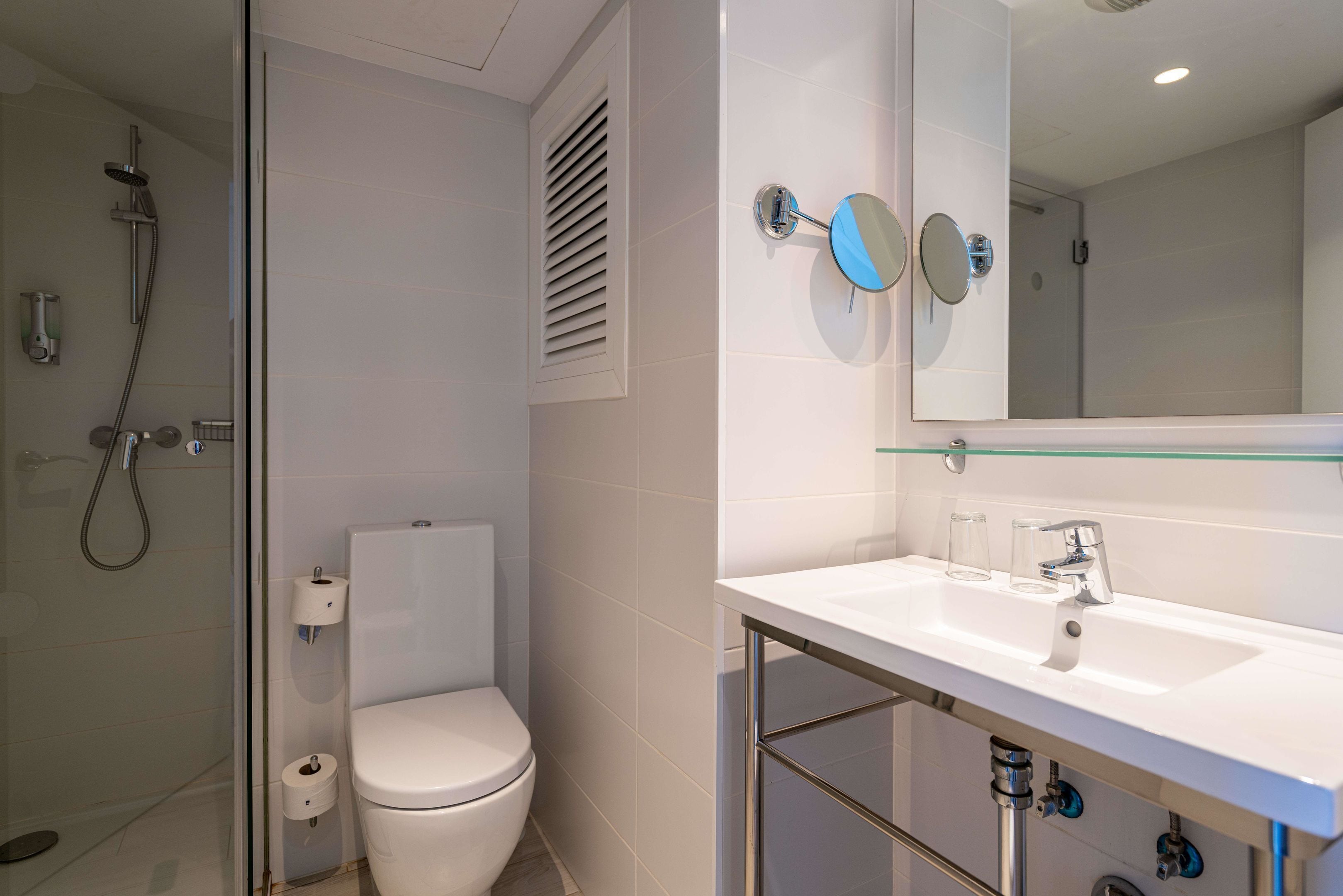 Un baño moderno con cabina de ducha de vidrio, inodoro blanco, lavabo con espejo y dispensador de papel higiénico.