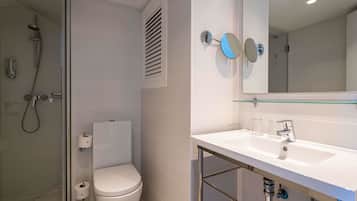 Un baño moderno con cabina de ducha de vidrio, inodoro blanco, lavabo con espejo y dispensador de papel higiénico.