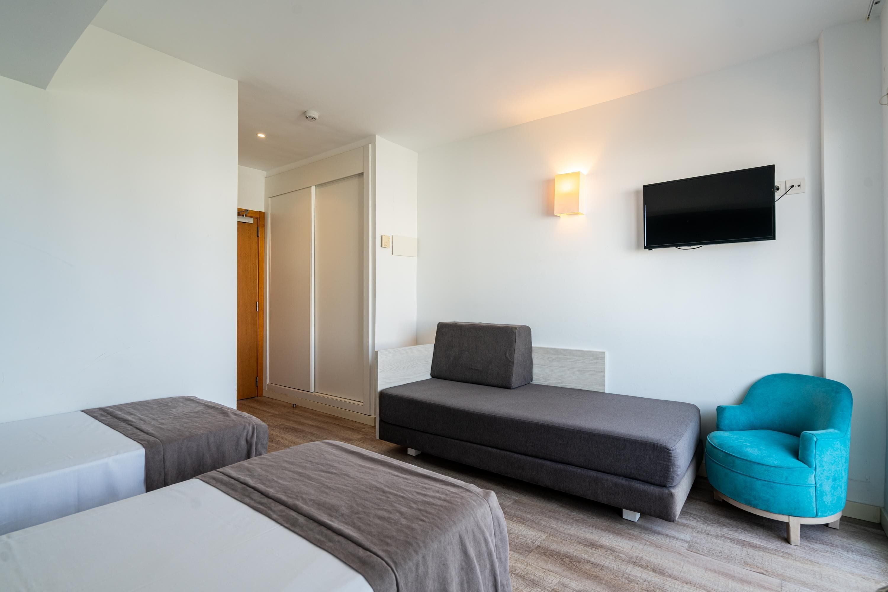 Una habitación de hotel con dos camas, un sofá, un televisor y una silla.