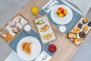 A breakfast table with various pastries, a bowl of fruit, and glasses of juice. - Hotel THB Niagara - Adults Only (Palma de Mallorca)