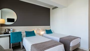 Una habitación de hotel con dos camas individuales, un escritorio con silla, un espejo y un televisor en la pared.