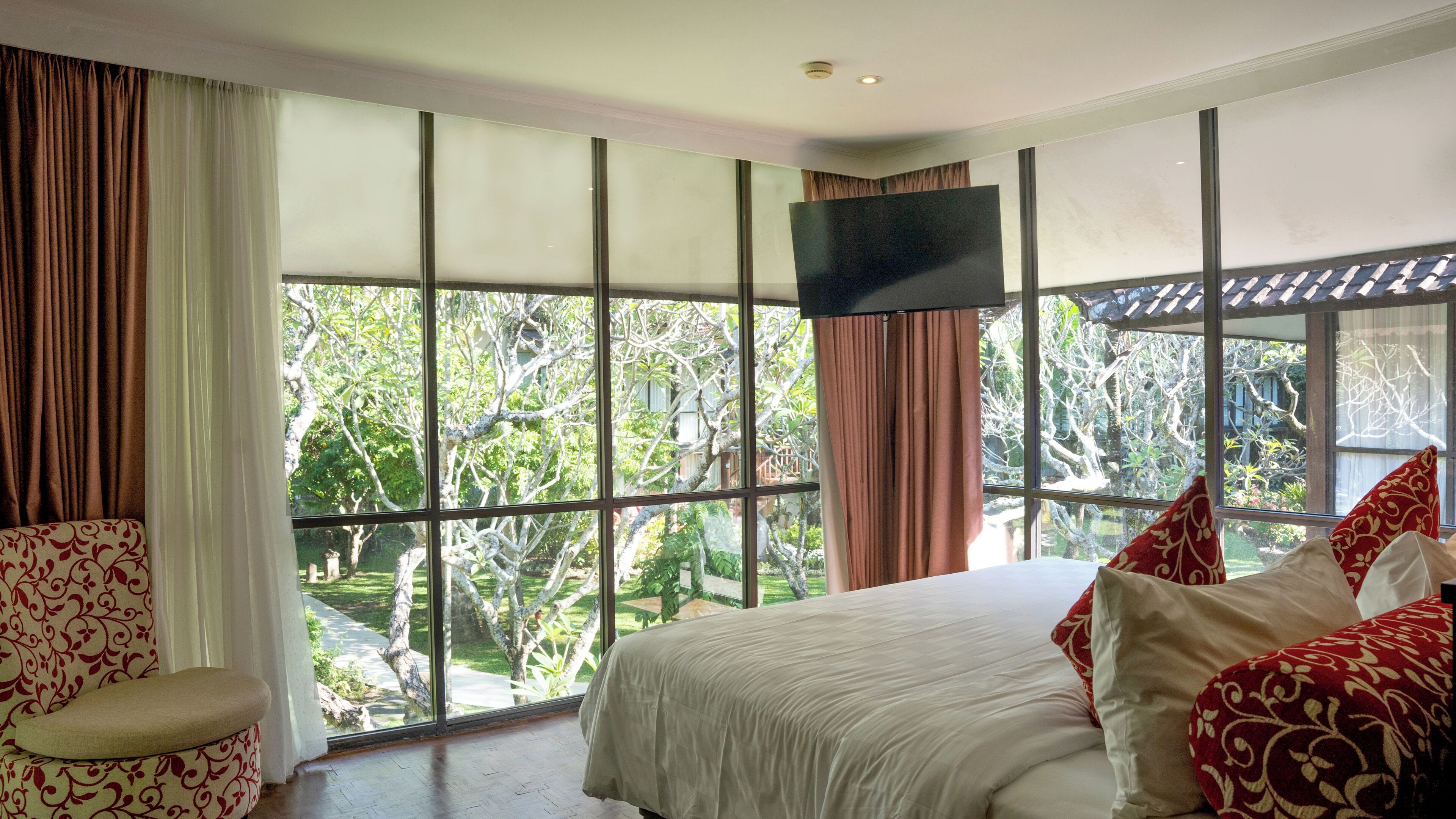 A bedroom with a large window, a bed, and a TV.