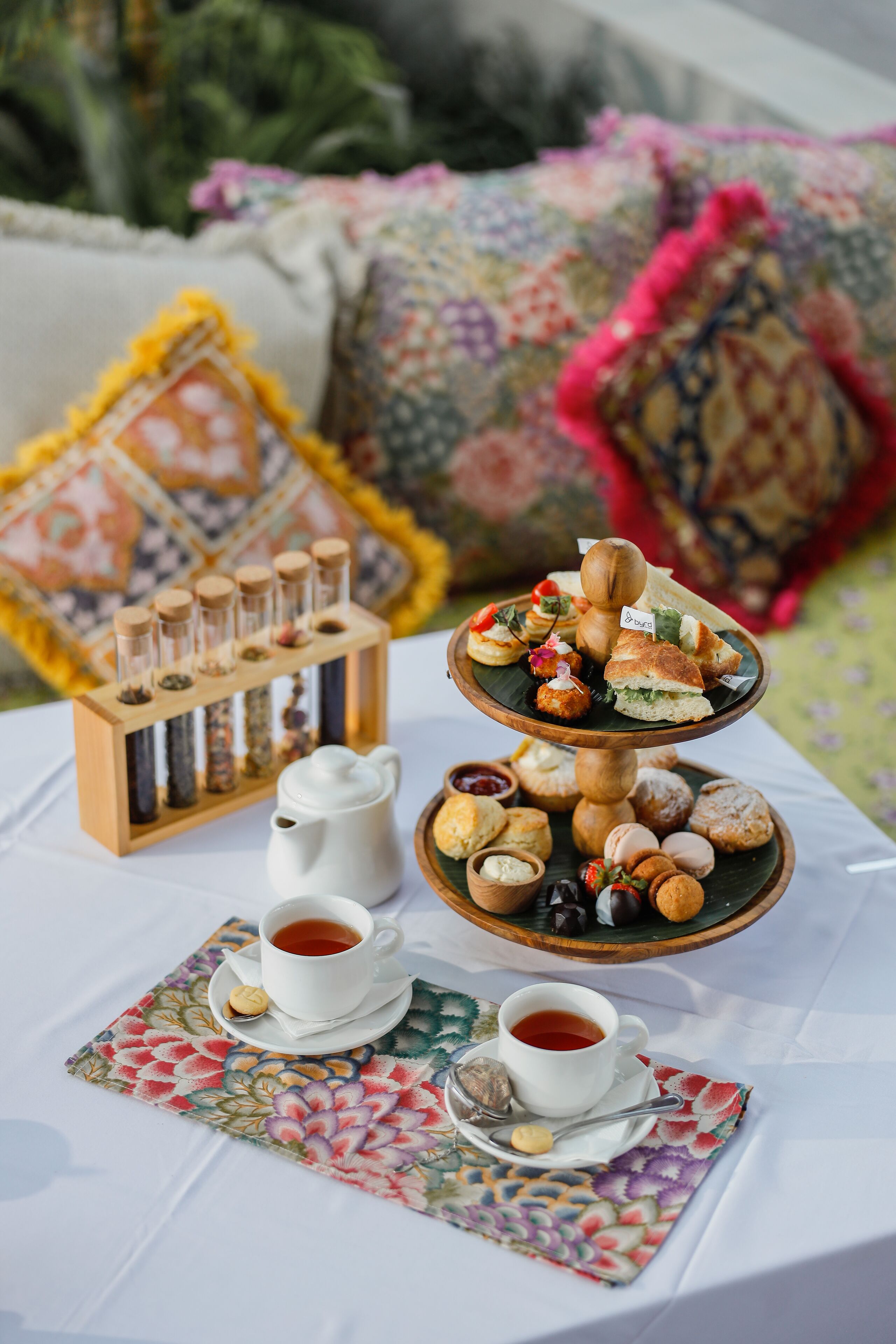 Una mesa servida con un expositor escalonado para postres, un juego de té y un mantel individual con motivos florales.