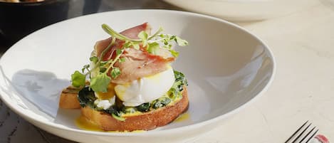 A table with three plates of food, including toast with greens and eggs, and bowls of soup and salad.
