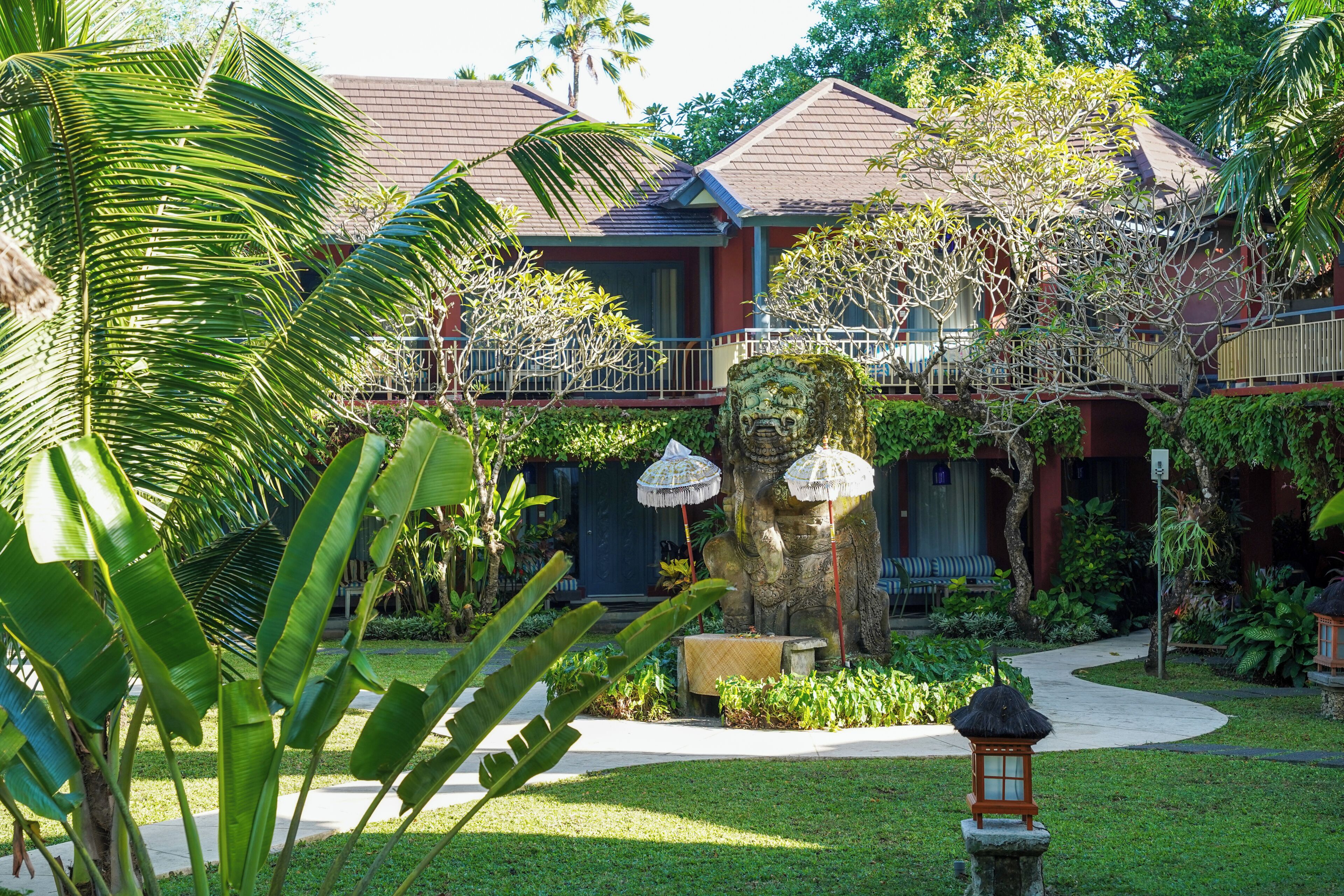 Un resort tropical con una estatua de león de piedra, abundante vegetación y un paseo cubierto.