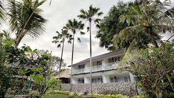 Um edifício de dois andares com varanda, cercado por vegetação exuberante e palmeiras.