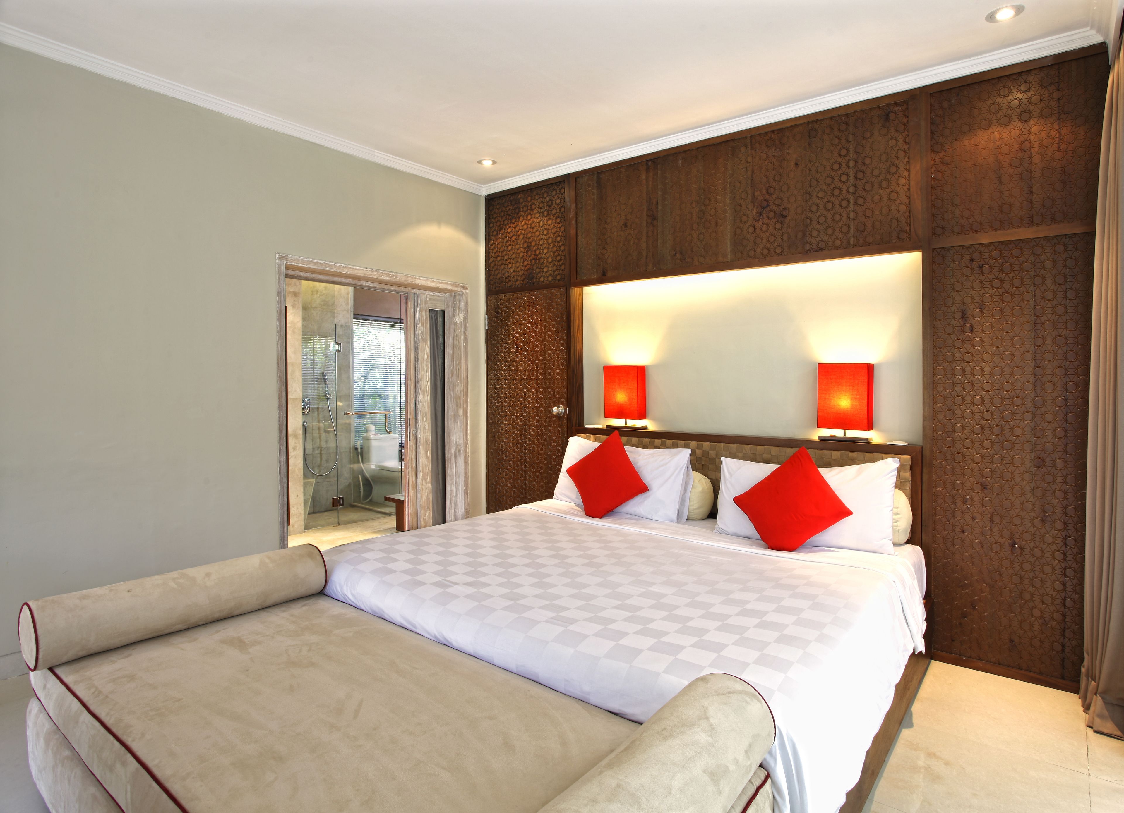 A hotel room with a large bed, two bedside lamps, a wooden headboard, and a glass shower enclosure.