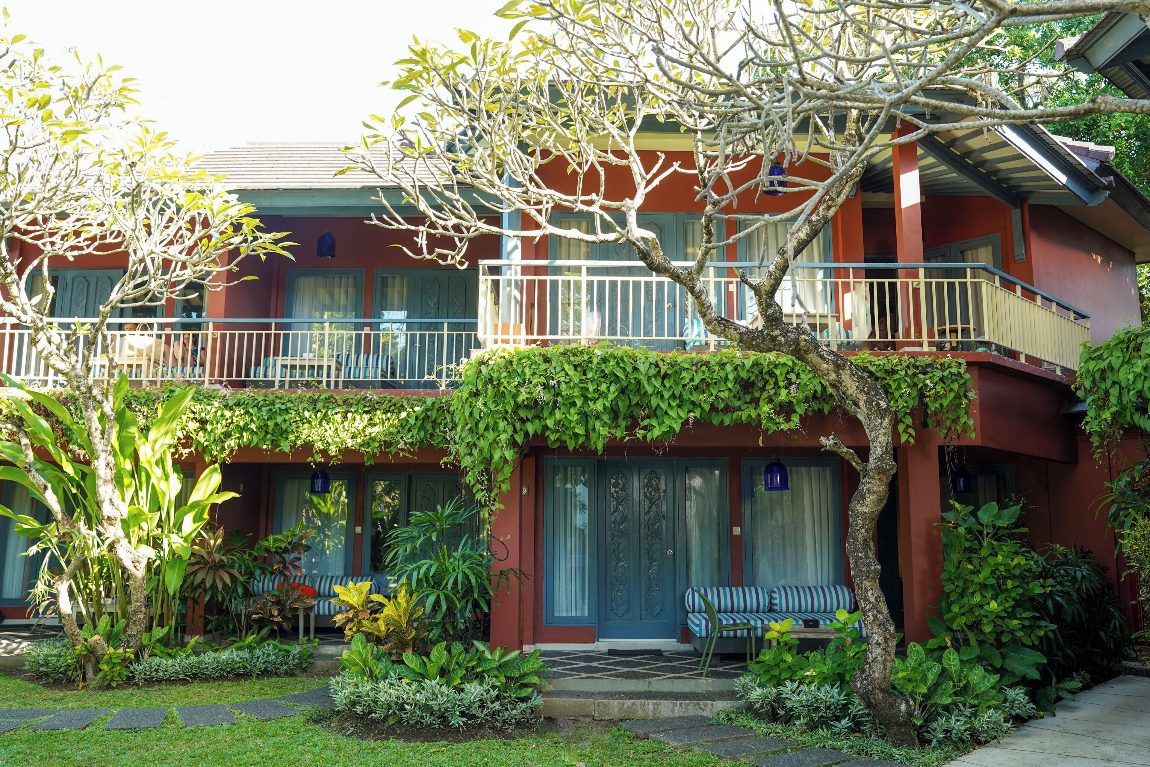 A two-story building with a balcony, a covered entrance, and a garden with various plants.
