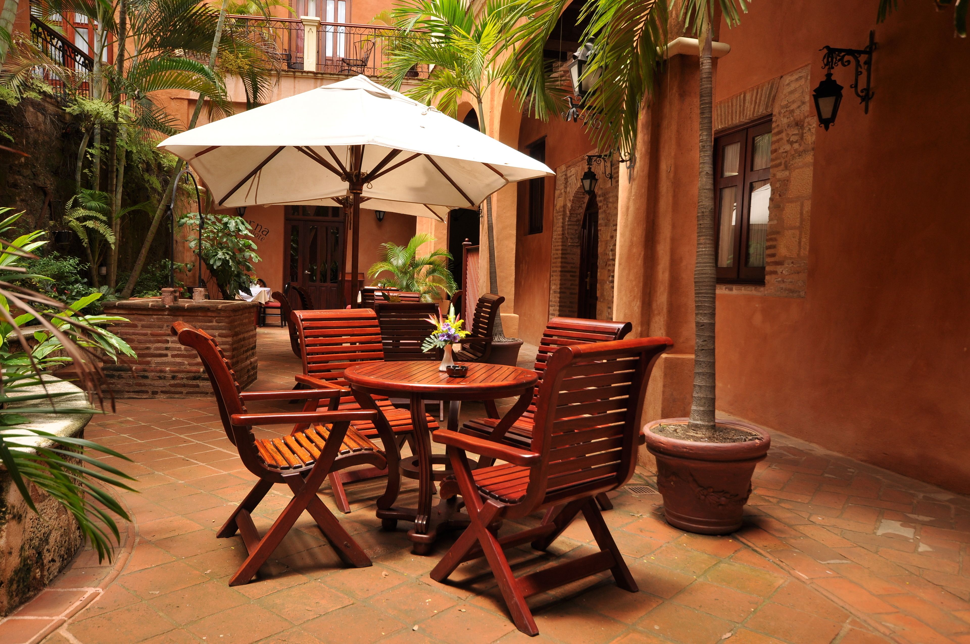 Un patio con muebles de madera, una sombrilla grande y plantas en macetas.