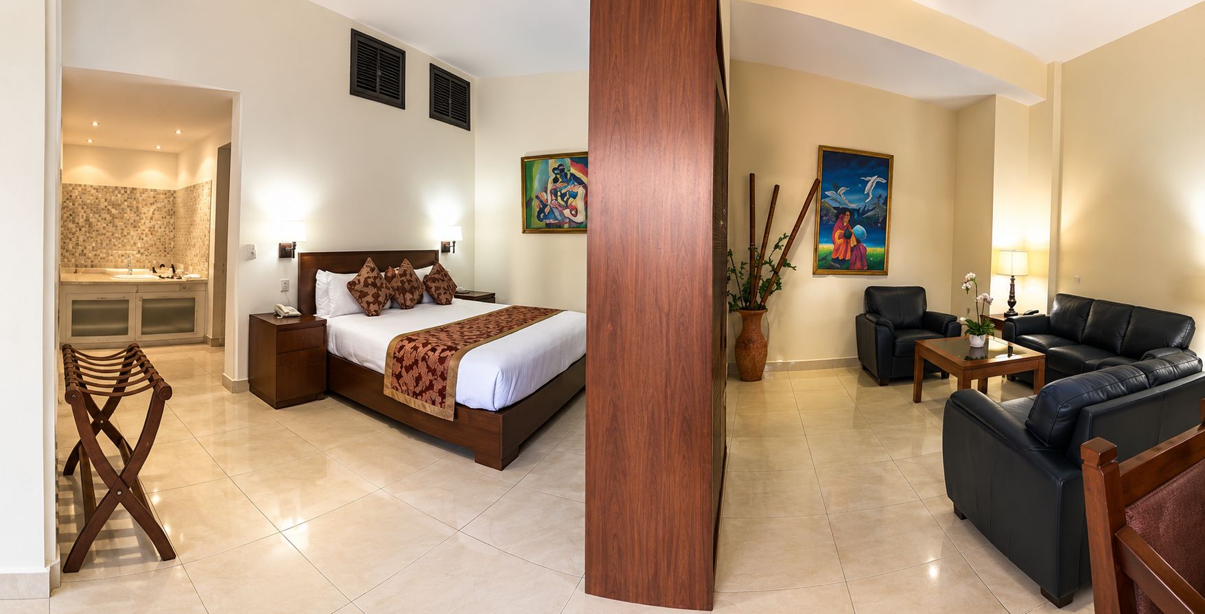 A hotel room with a bed, a seating area with a sofa and chairs, a small table, and a painting on the wall.