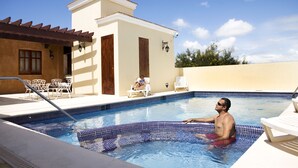 A swimming pool with a tiled edge, lounge chairs, and a building with a tiled roof and doors. - Boutique Hotel Palacio (Santo Domingo)