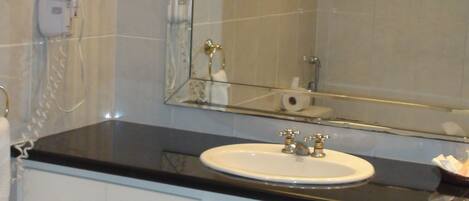 A bathroom with a white sink, a mirror, a towel rack, and a toilet paper holder.