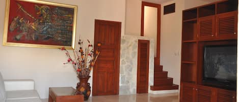 Una sala de estar con un sofá, un televisor, un cuadro y una escalera que lleva a otra habitación.