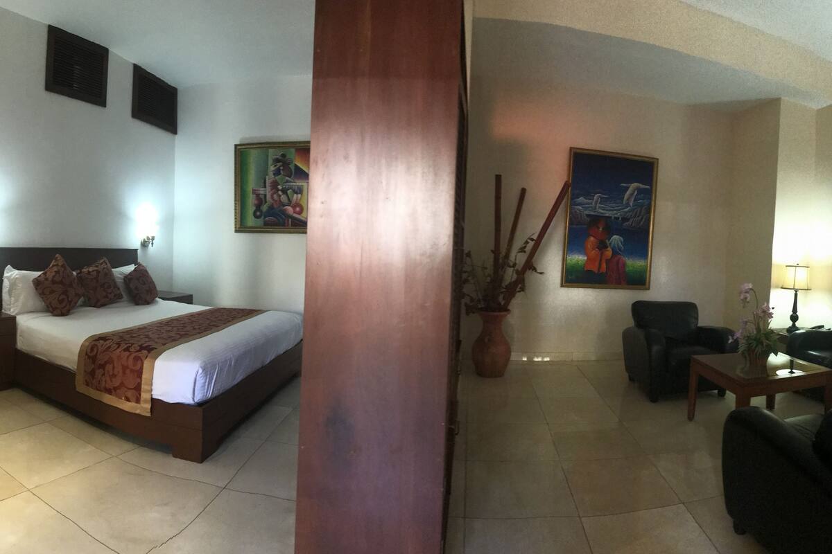 Een hotelkamer met een bed, nachtkastjes, een zithoek met een bank en stoelen, een klein tafeltje en een tv aan de muur.