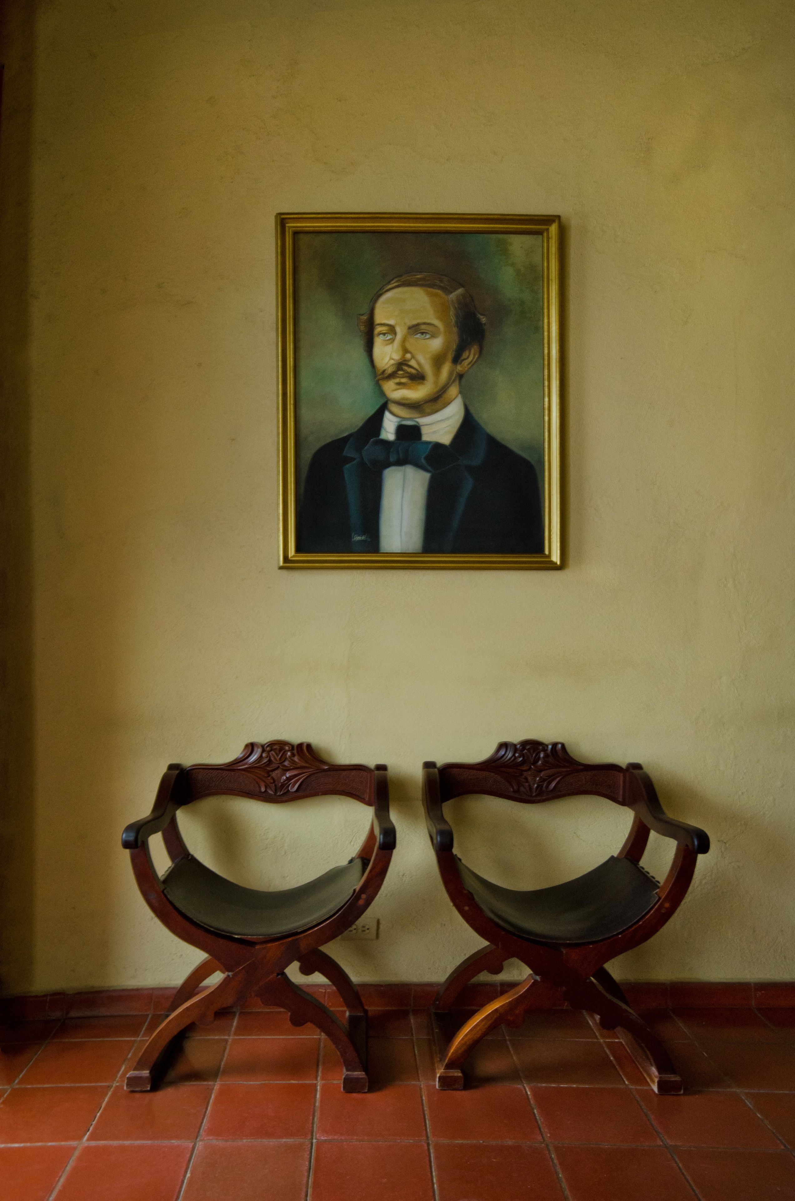 Een kamer met een ingelijst portret aan de muur en twee houten stoelen met gebogen rugleuningen.