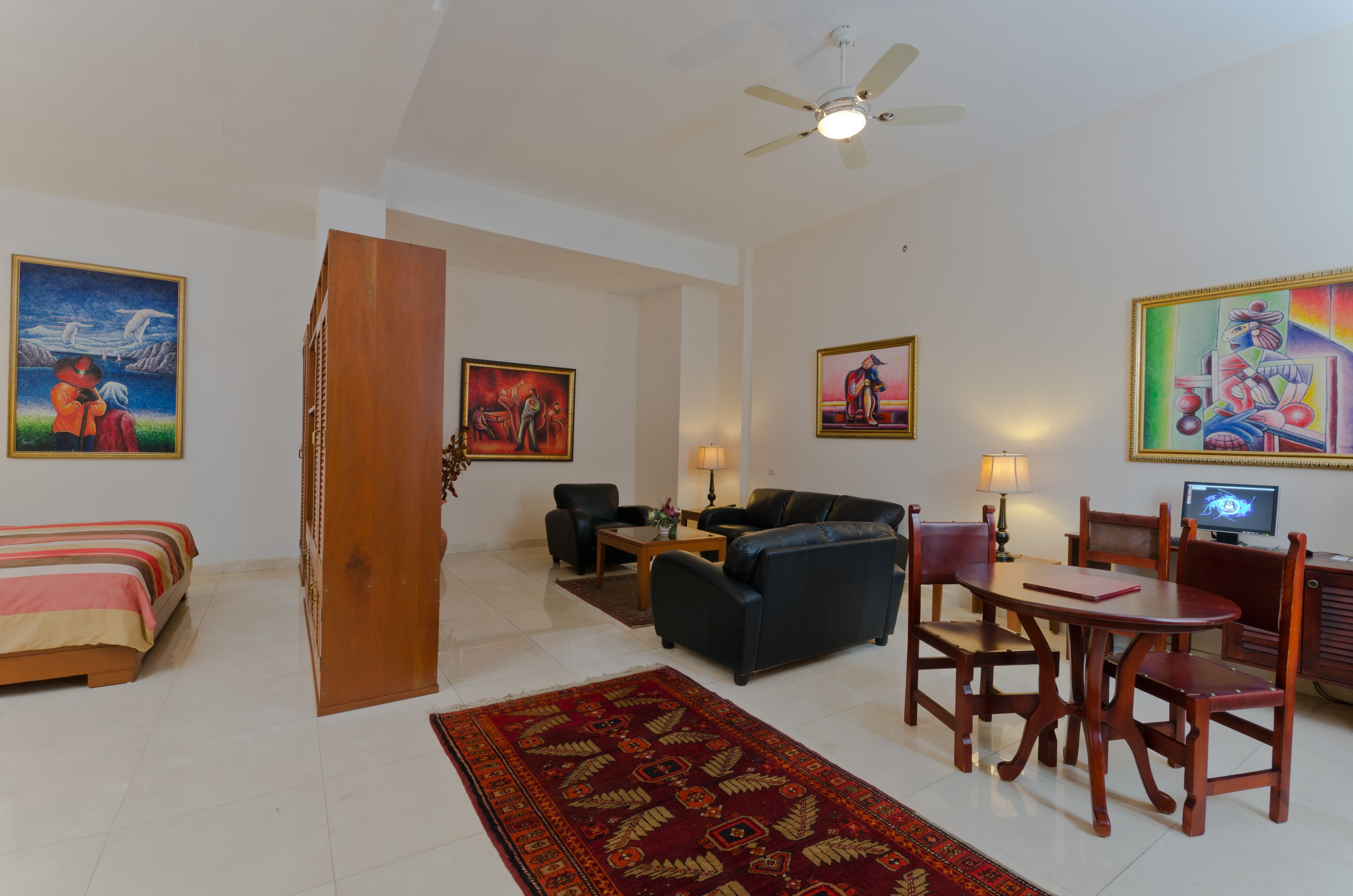 Sala de estar com sofá, cadeiras, mesa de centro e televisão. Há quadros nas paredes e um ventilador de teto.
