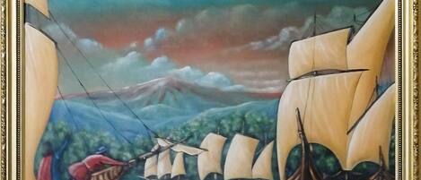 A framed painting of a seascape with multiple sailing ships and a mountainous background.