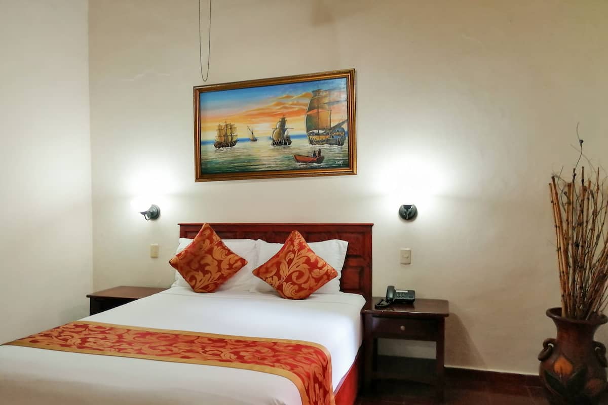 Een hotelkamer met een bed, een nachtkastje, een telefoon en een schilderij van schepen aan de muur.