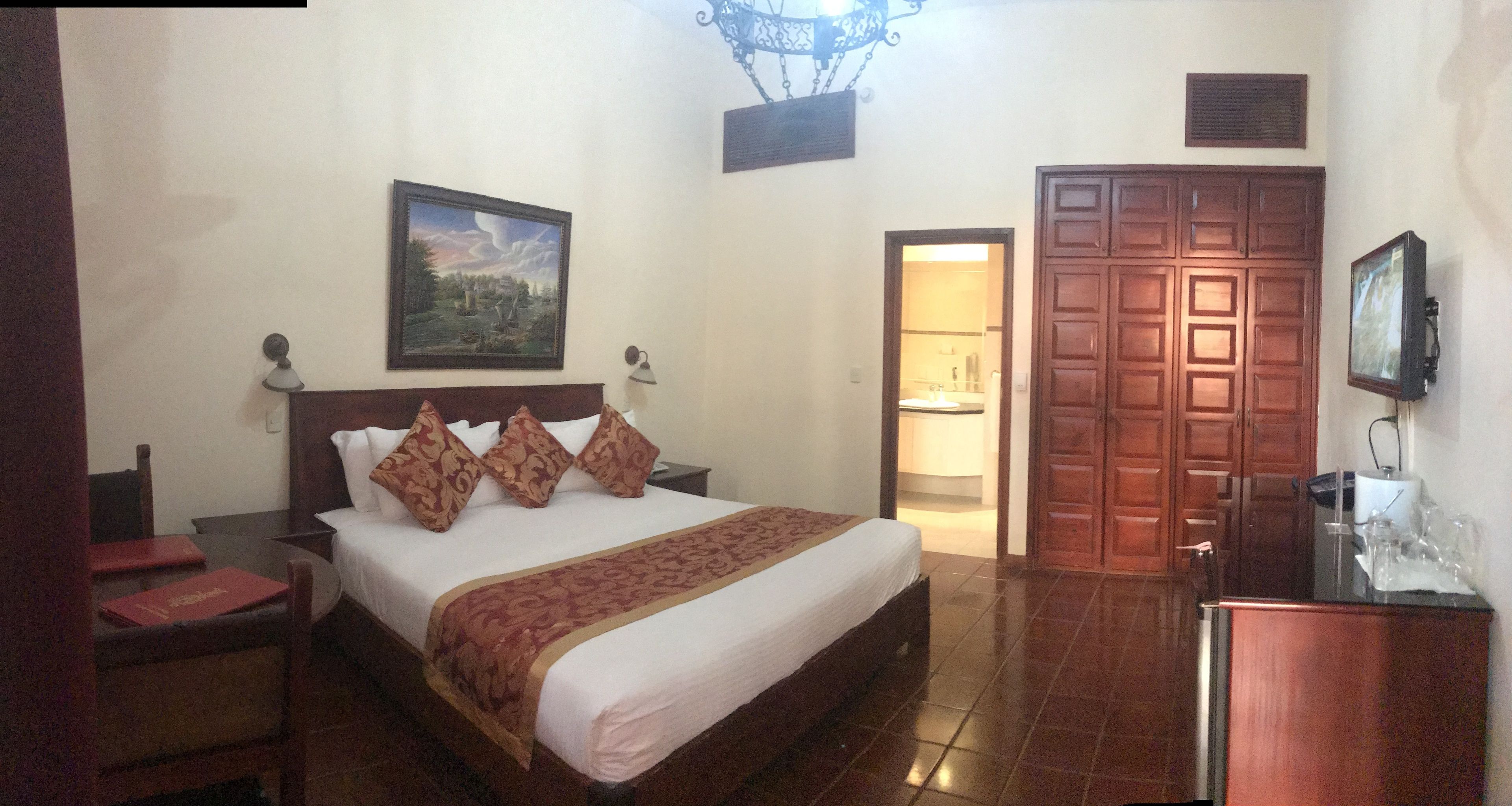 A hotel room with a large bed, a television, a wooden wardrobe, and a painting on the wall.