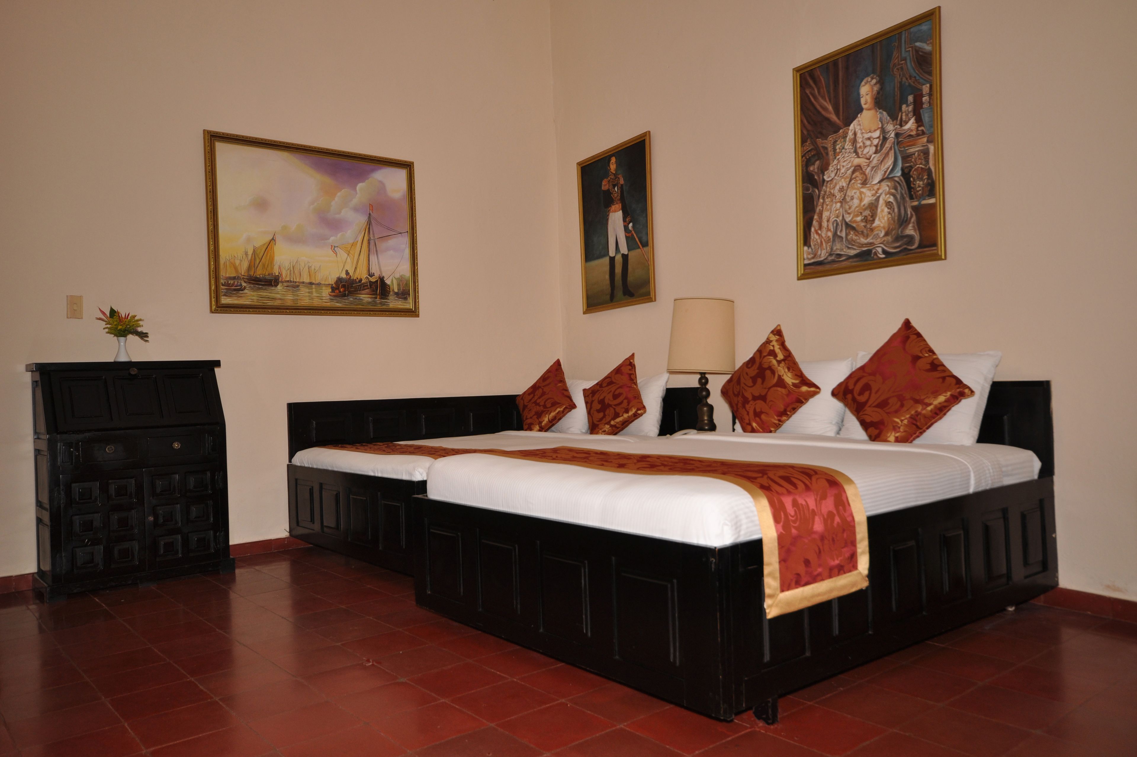 A double bed with a white and red bedspread, two nightstands, a lamp, and a dresser with a vase of flowers.