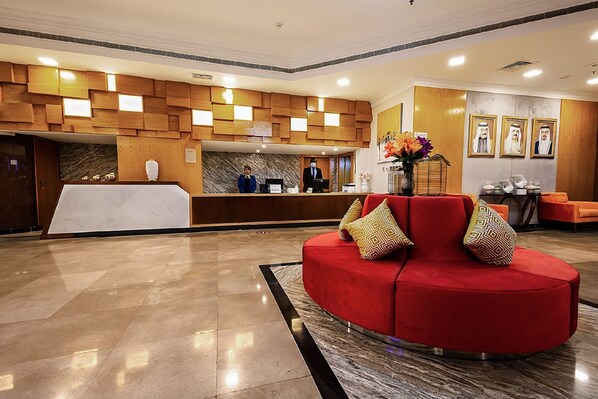 Un vestíbulo de hotel con mostrador de recepción, un sofá rojo y suelo de mármol.