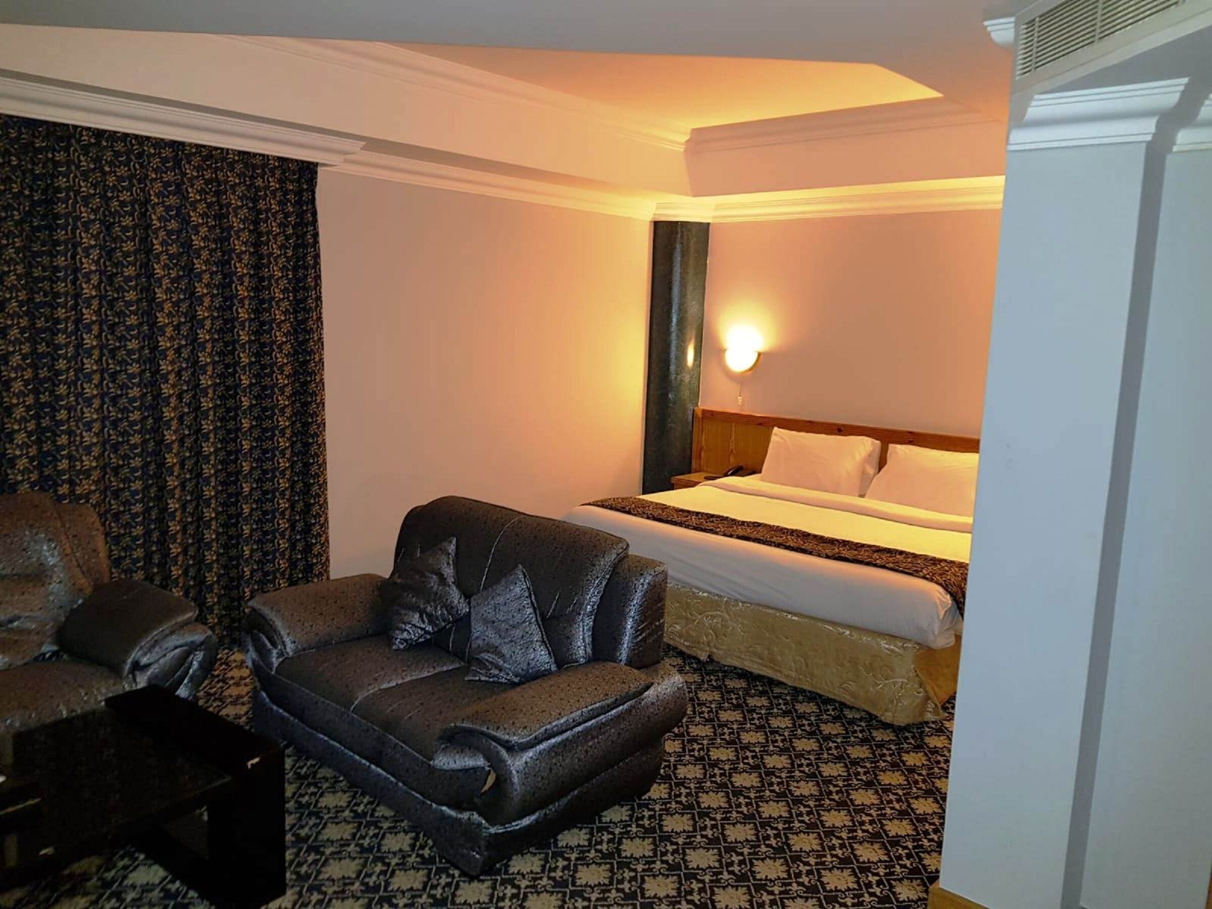 Habitación de hotel con cama, sillón de cuero, mesita y alfombra estampada.