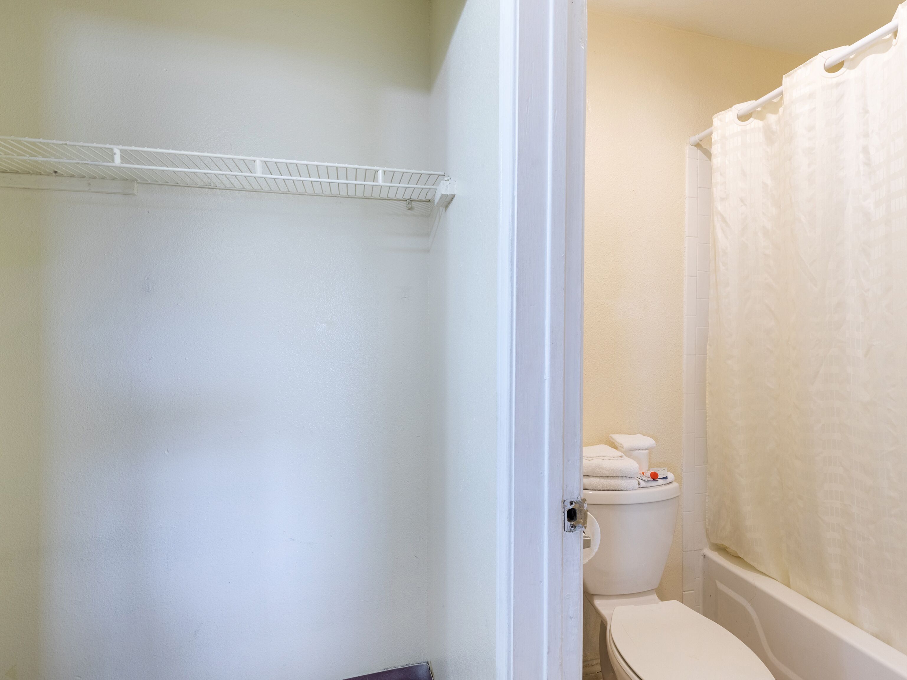 A bathroom with a toilet, a shower curtain, and a white shelf.