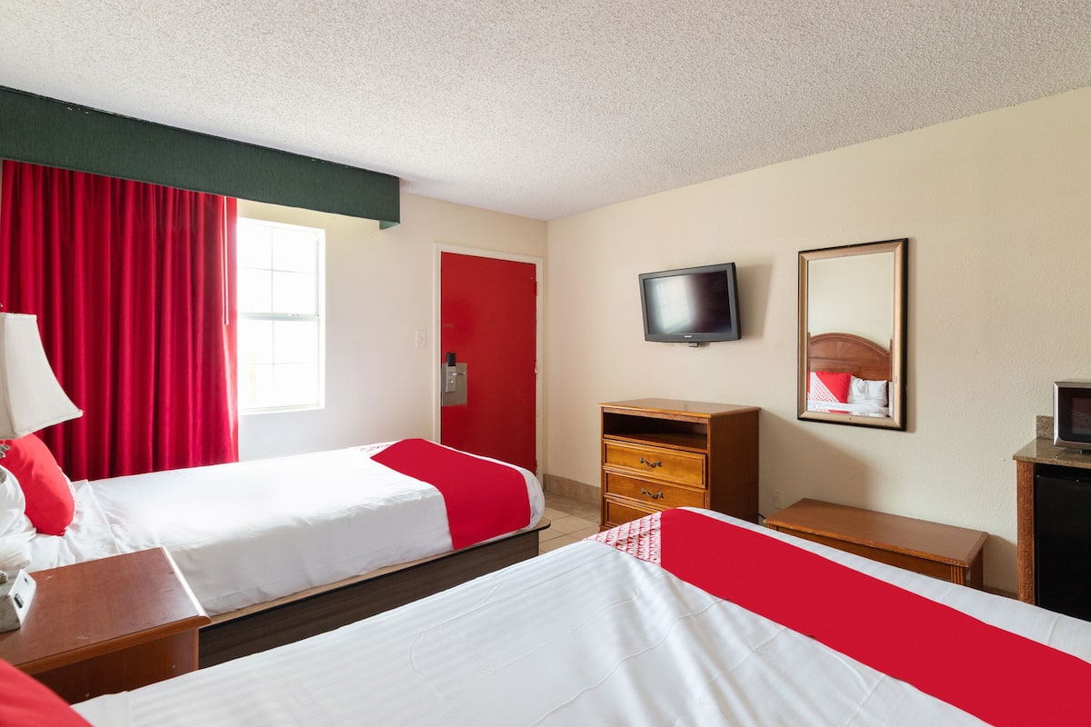 Quarto de hotel com duas camas, televisão, escrivaninha e espelho.