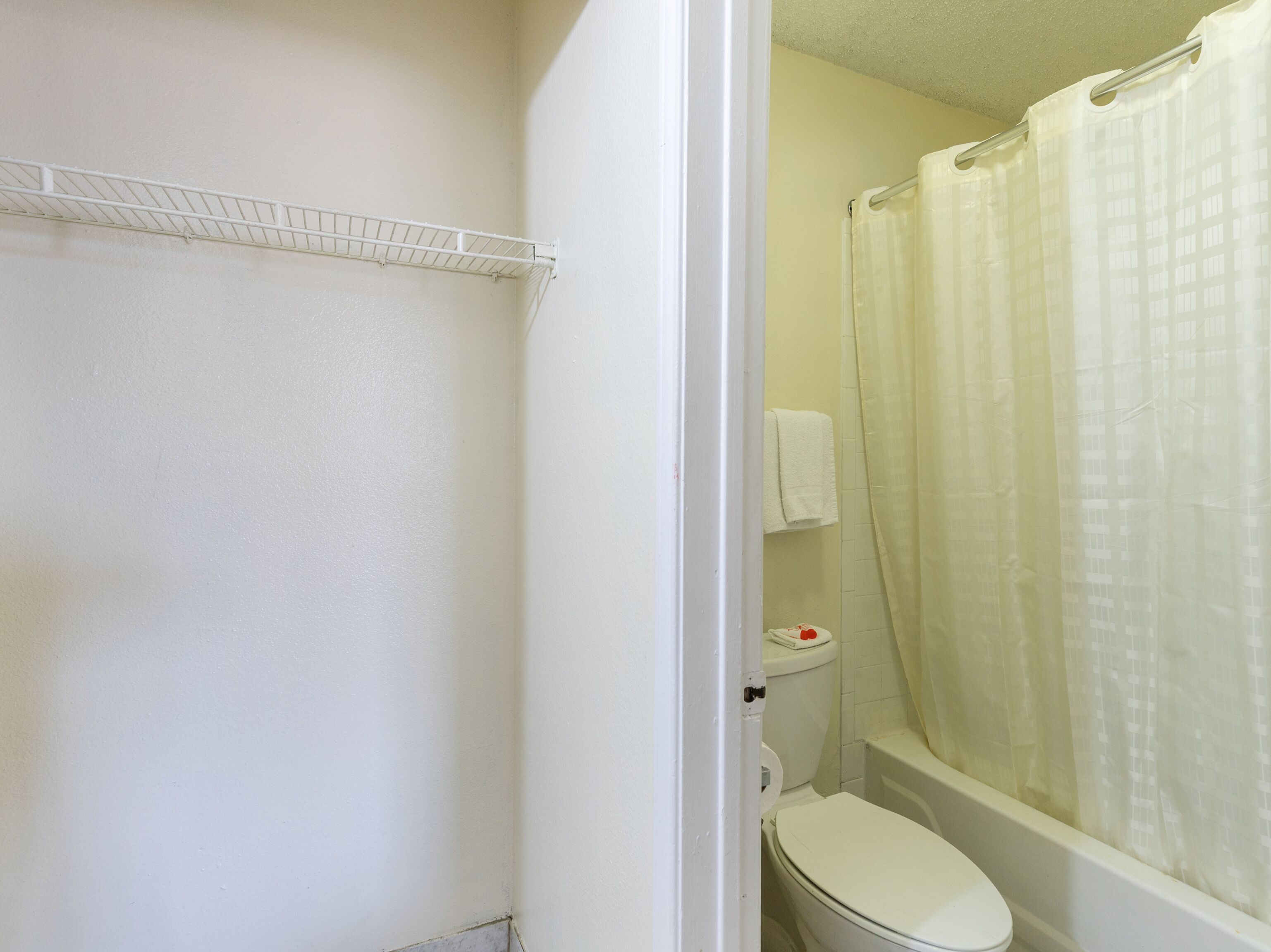 A bathroom with a toilet, a shower curtain, and a shelf above the toilet.