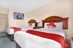 A hotel room with two beds, each with a red and white bedspread, a wooden headboard, and a wall-mounted lamp.